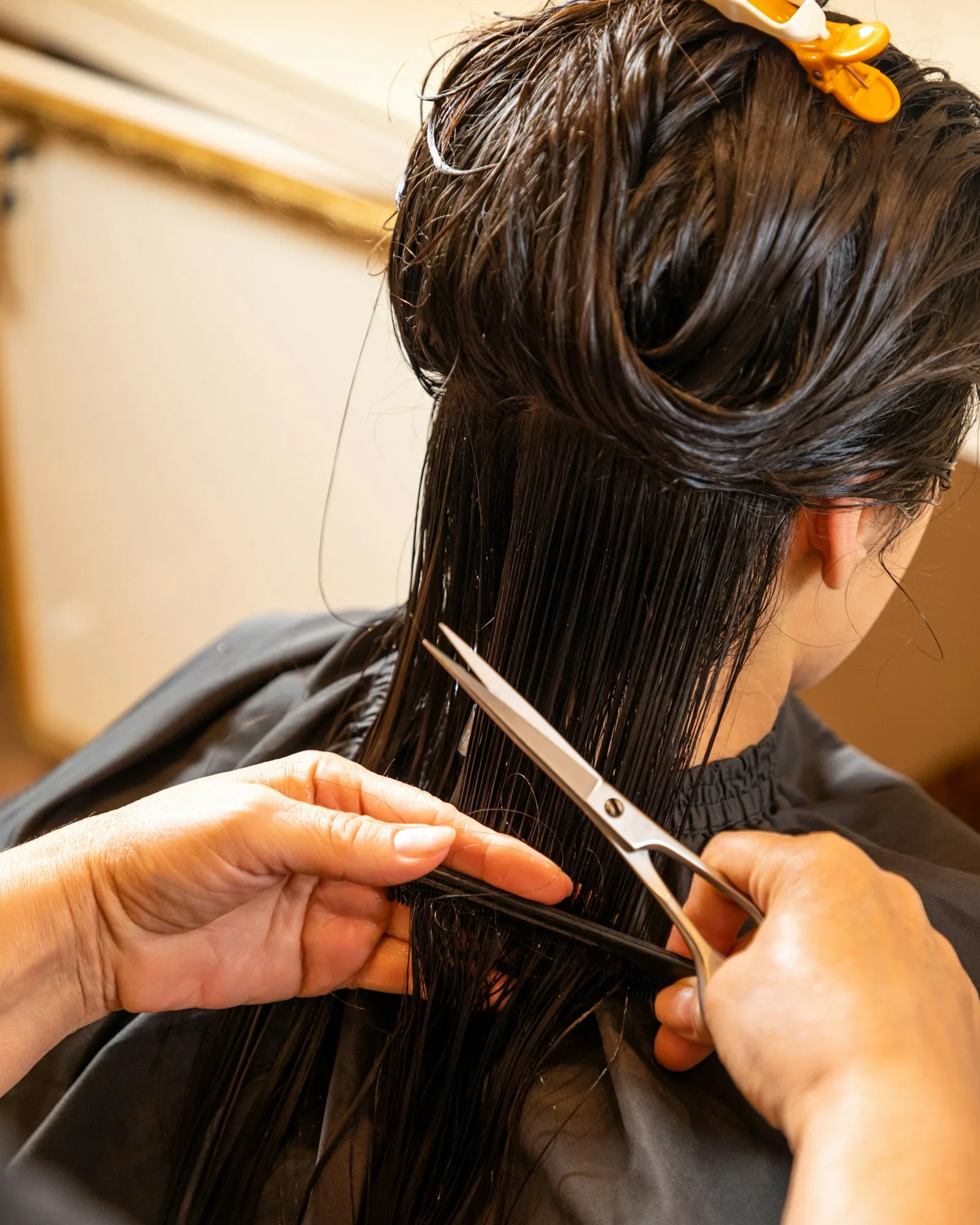 Mains d'un coiffeur coupant aux ciseaux les longueurs d'une chevelure brune sous une cape noire